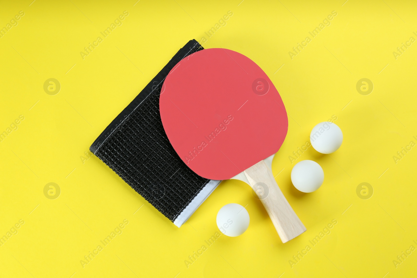 Photo of Ping pong racket, net and balls on yellow background, flat lay