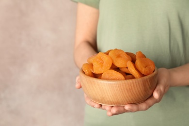 Photo of Woman holding bowl with dried apricots on color background, space for text. Healthy fruit