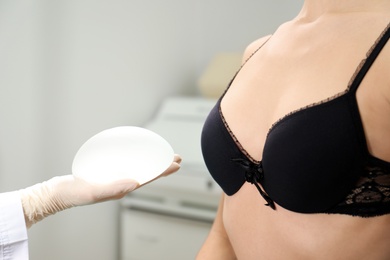 Photo of Doctor showing silicone implant for breast augmentation to patient in clinic, closeup. Cosmetic surgery