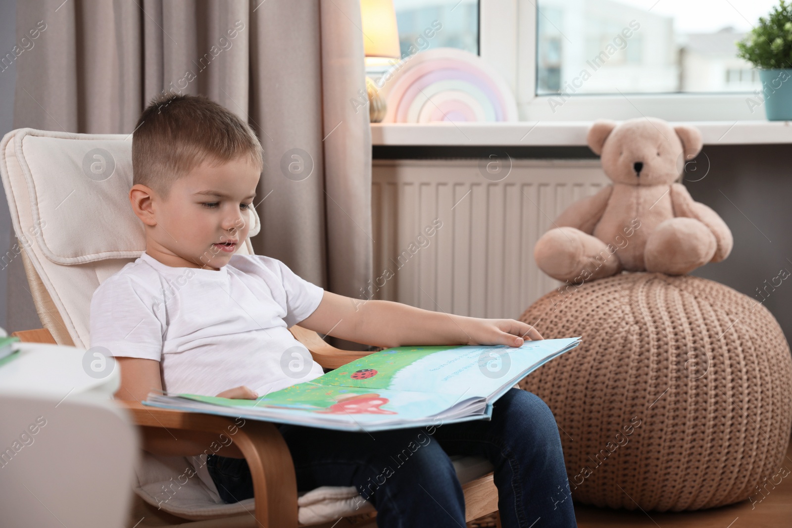 Photo of Cute little boy reading book at home, space for text