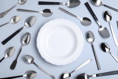 Composition with empty plate and metal spoons on white background, top view