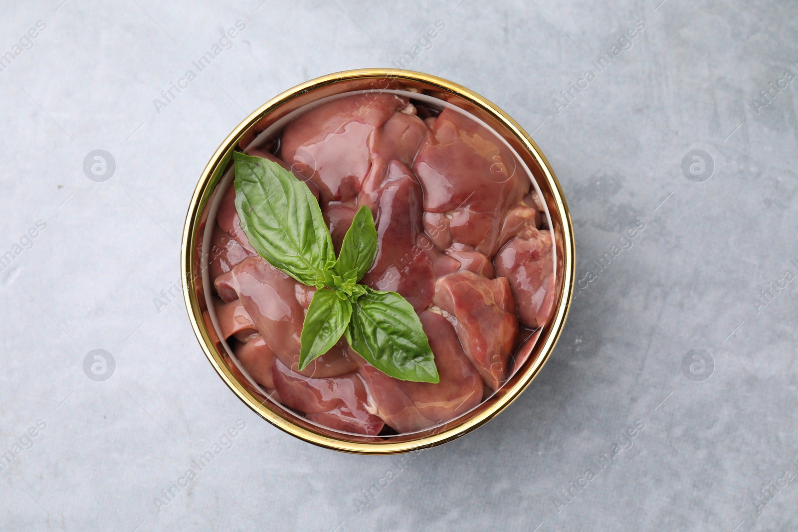 Photo of Bowl with raw chicken liver and basil on light grey table, top view