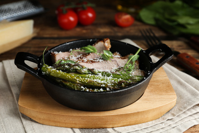 Photo of Tasty meat served with asparagus and sprouts in portioned frying pan on table