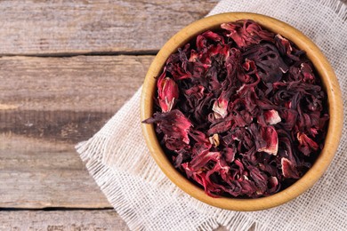 Photo of Dry hibiscus tea in bowl on wooden table, top view. Space for text