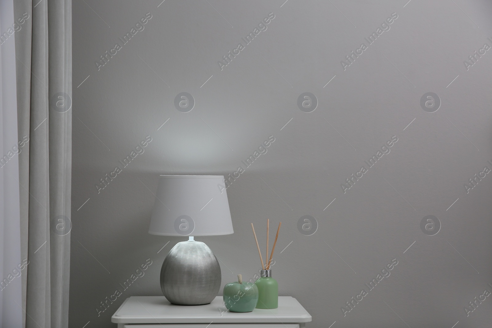 Photo of Wooden nightstand with decor and modern lamp near light grey wall, space for text. Interior element