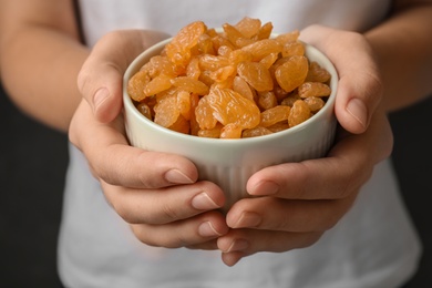 Photo of Woman holding bowl with raisins on black background, closeup