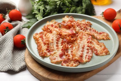 Photo of Delicious fried bacon slices and other products on white wooden table, closeup