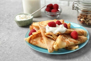 Photo of Thin pancakes with berries and sour cream on plate, closeup