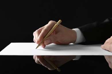 Photo of Woman writing with pen on sheet of paper at glass table, closeup