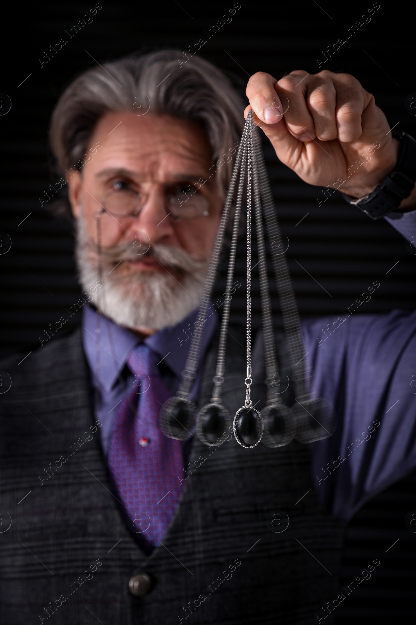 Image of Hypnosis session. Man swinging pendant on black background, motion effect