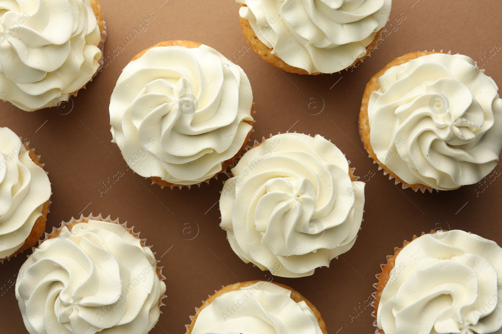 Photo of Tasty vanilla cupcakes with cream on dark beige background, top view