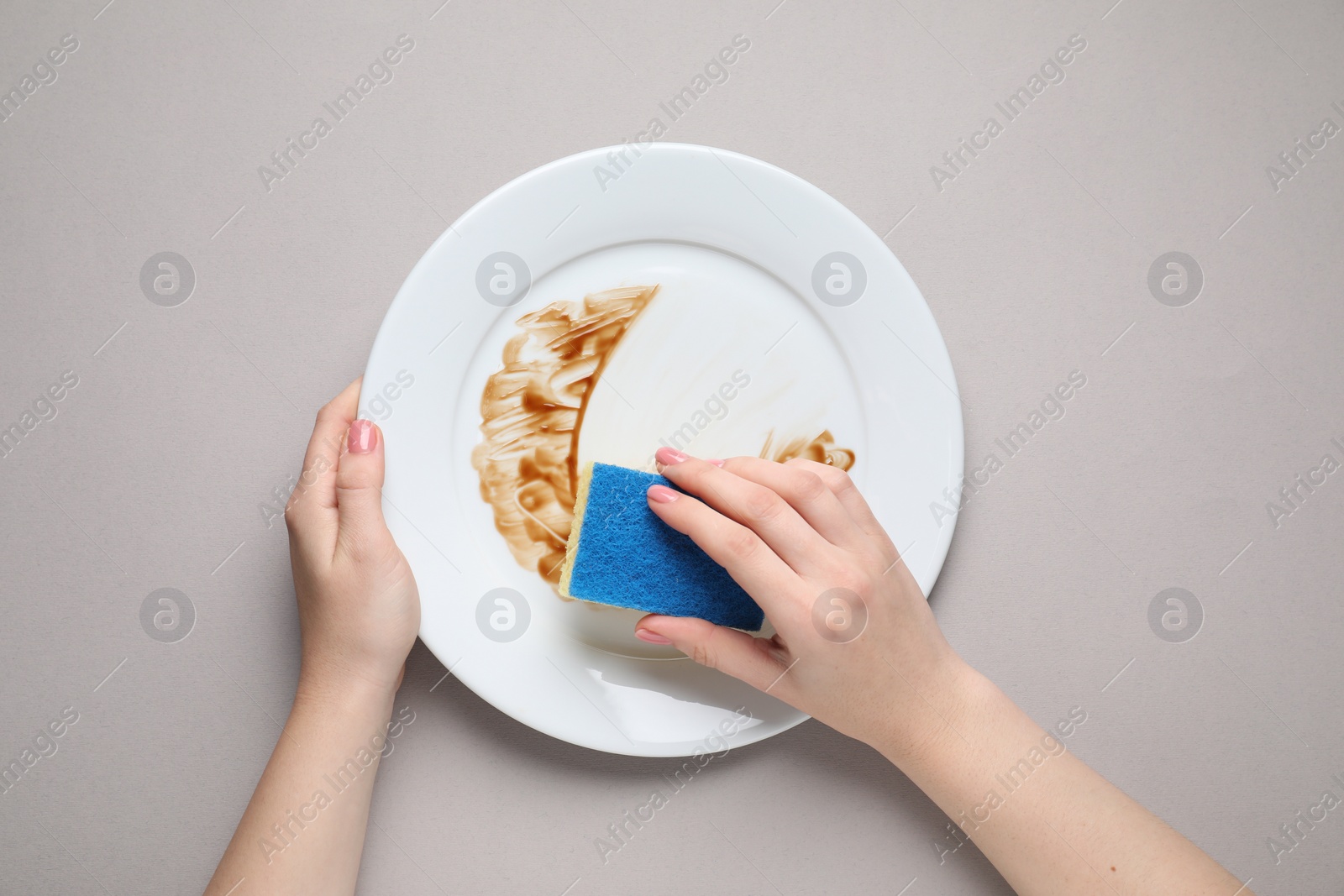 Photo of Woman washing dirty plate with sponge on light grey background, top view