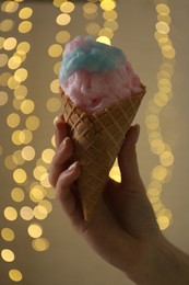 Photo of Woman holding waffle cone with cotton candy against blurred lights, closeup