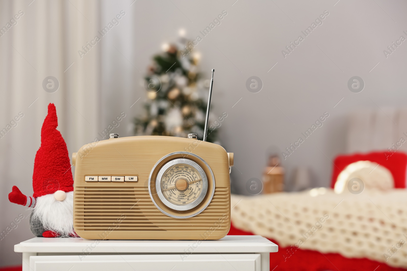 Photo of Stylish radio and Christmas gnome on white table in decorated bedroom