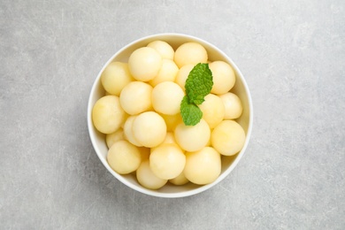 Photo of Melon balls and mint in bowl on light grey table, top view
