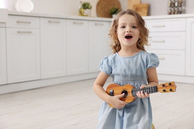 Photo of Little girl playing toy guitar in kitchen. Space for text