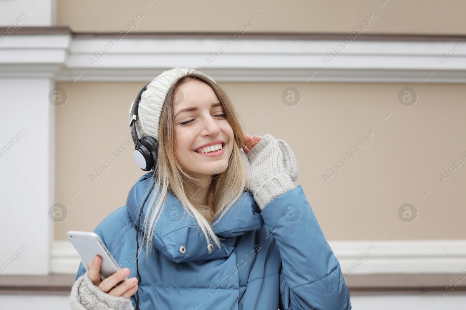 Photo of Young woman with headphones listening to music near light wall