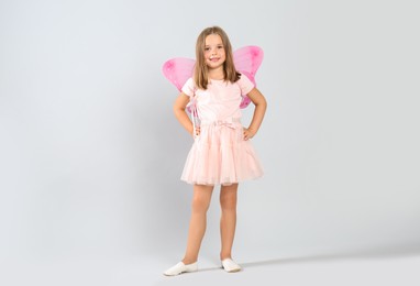 Cute little girl in fairy costume with pink wings and magic wand on light background