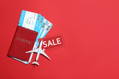 Photo of Flight tickets, passport, plane model and SALE card on red background, flat lay. Space for text