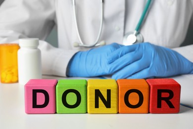 Word Donor made of wooden cubes. Doctor sitting at white table, closeup