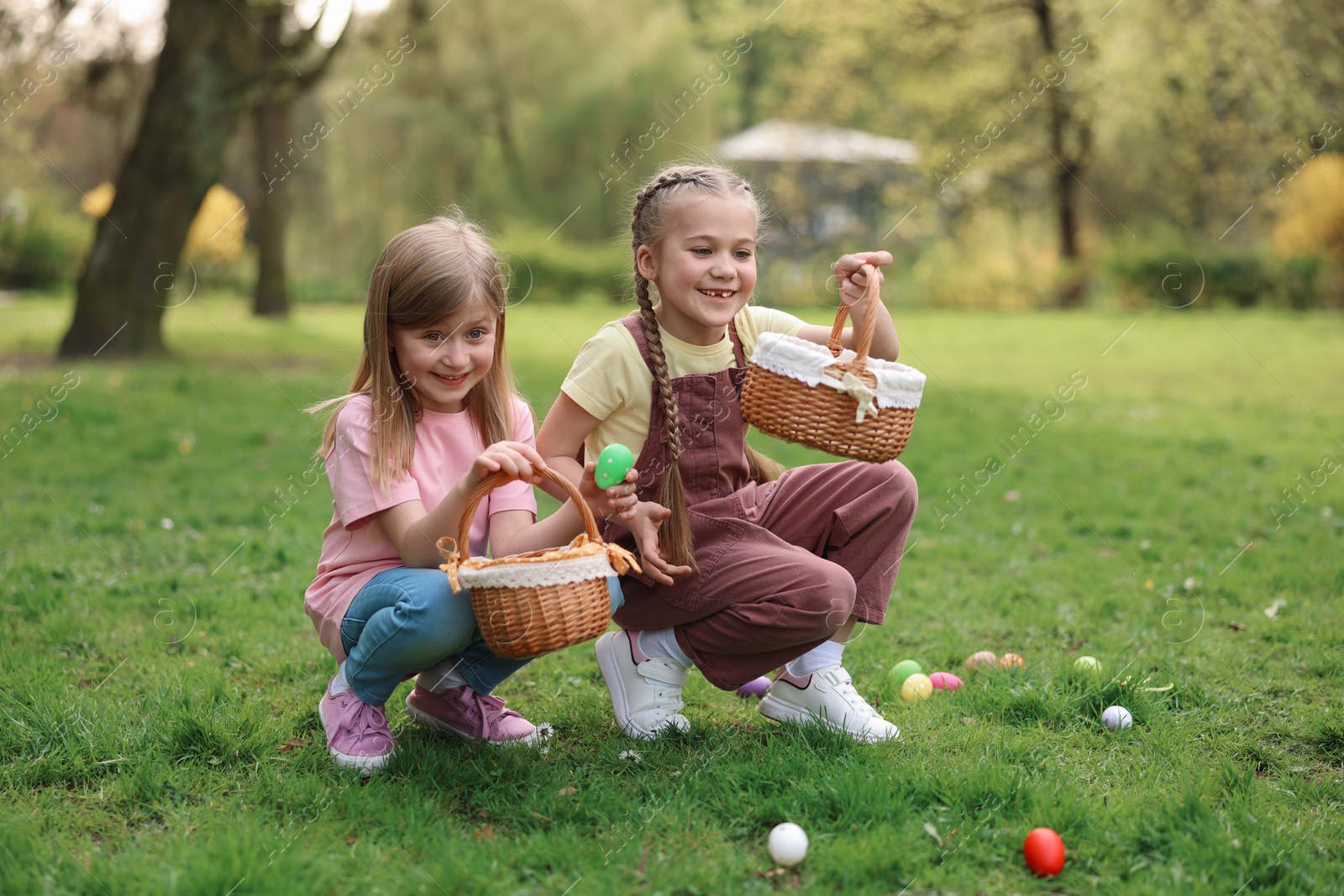 Photo of Easter celebration. Cute little girls hunting eggs outdoors