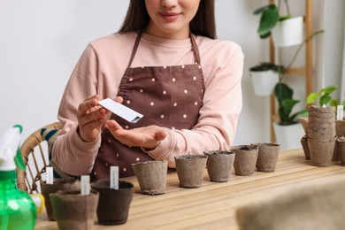 Woman planting vegetable seeds into peat pots with soil at wooden table indoors, closeup