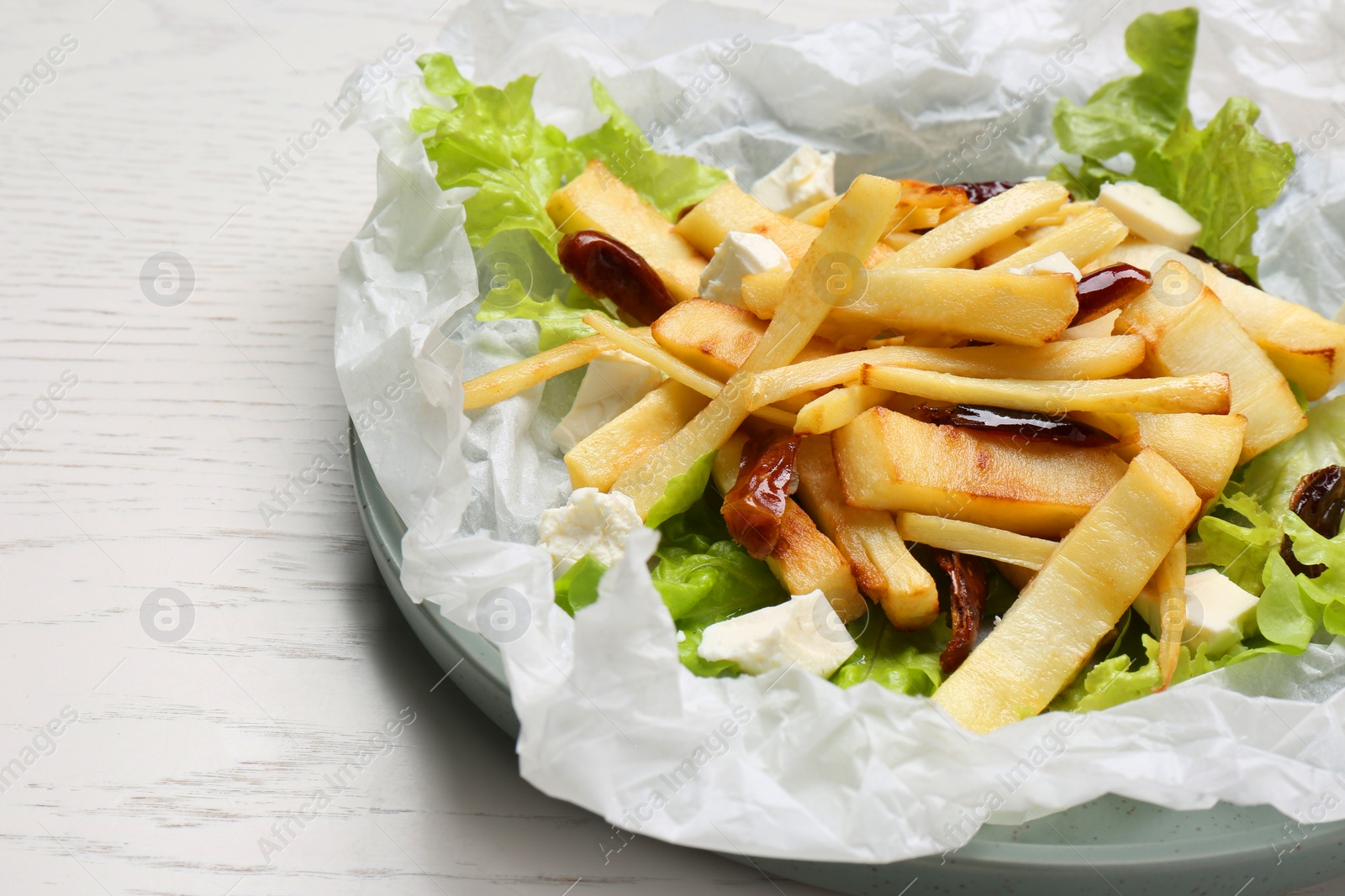 Photo of Delicious parsnip with lettuce, feta cheese and dates on white wooden table, closeup