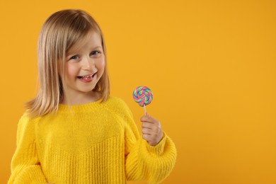 Photo of Happy girl with lollipop on orange background. Space for text