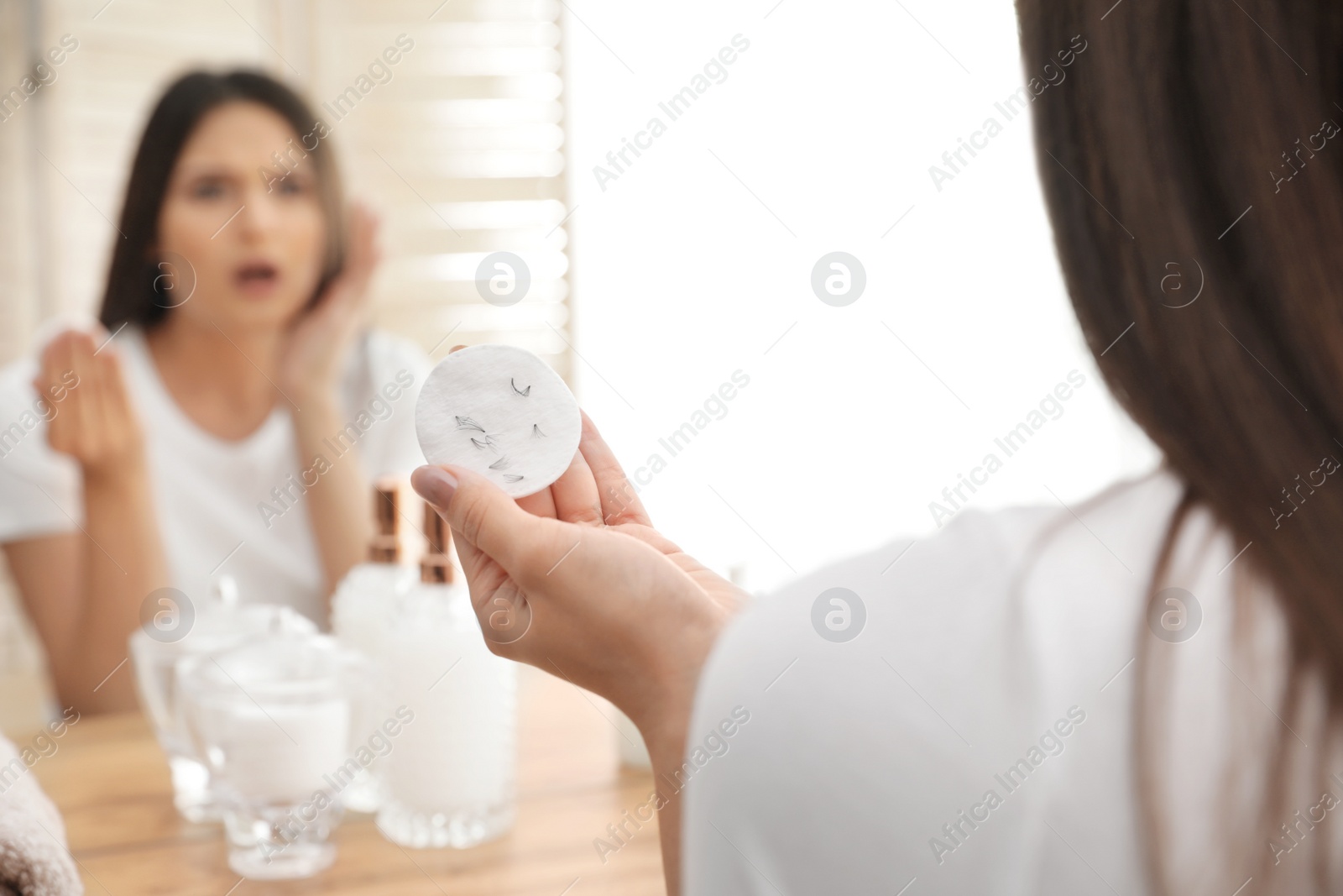 Photo of Beautiful woman holding cotton pad with fallen eyelashes near mirror indoors, closeup