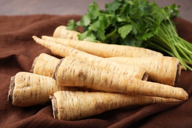 Photo of Whole raw parsley roots and fresh herb on brown fabric, closeup