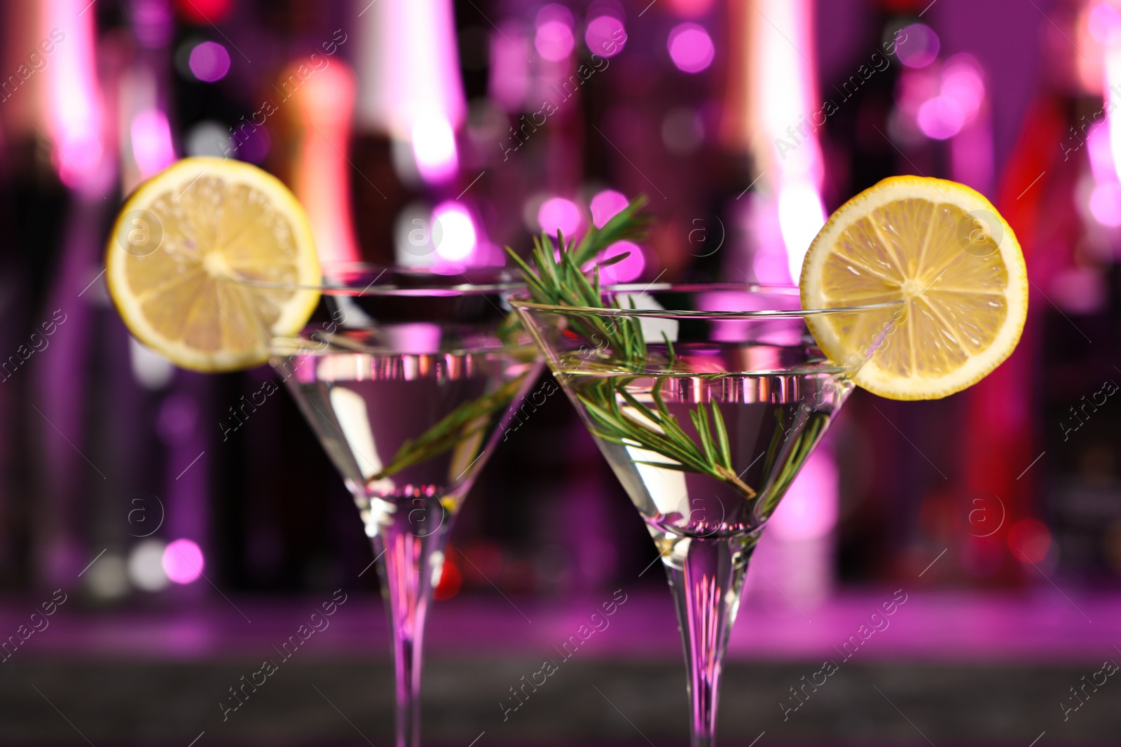 Photo of Martini glasses of refreshing cocktail, lemon slices and rosemary on blurred background