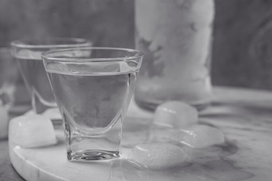 Photo of Shot glasses and bottle of vodka with ice cubes on marble board, closeup