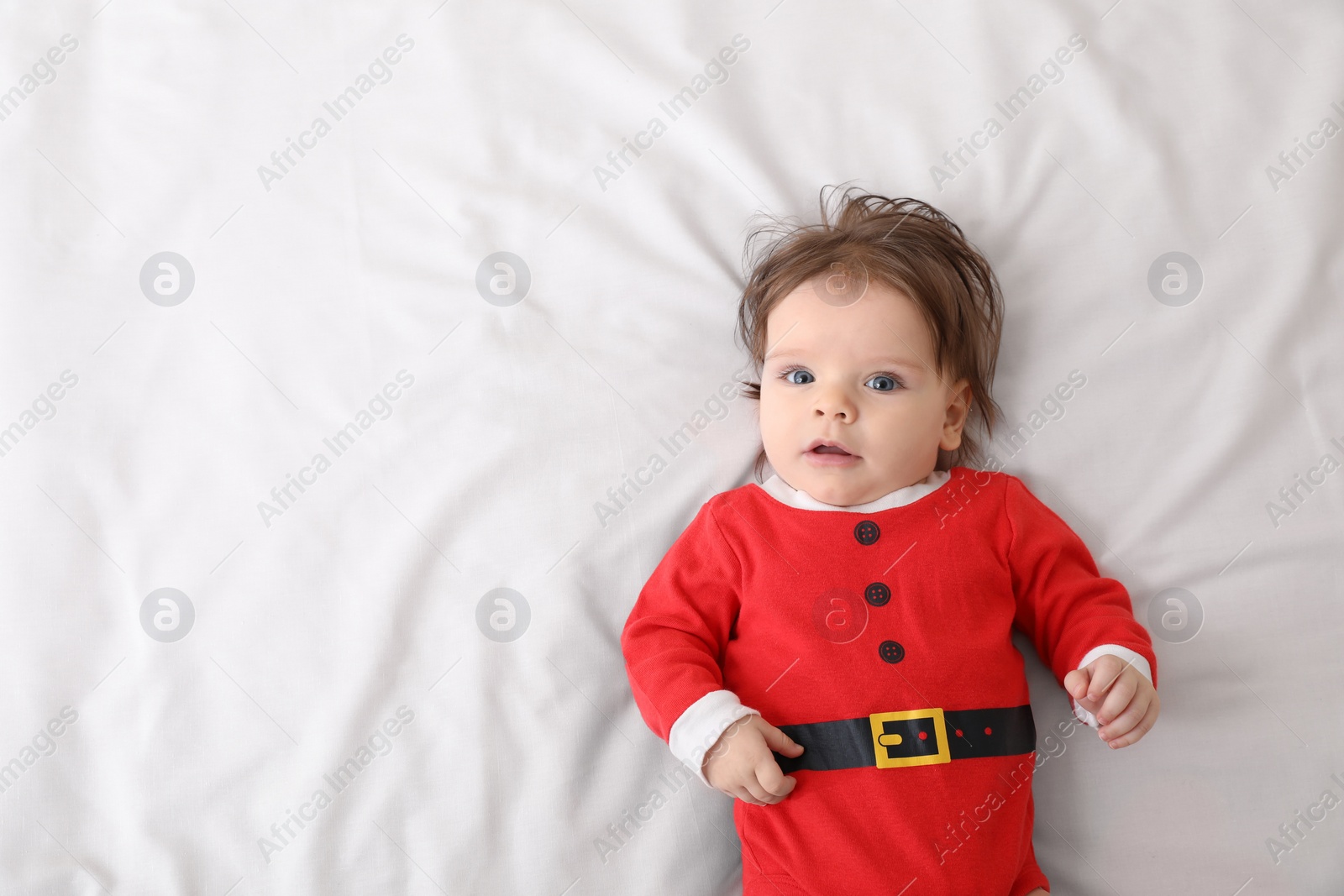 Photo of Cute baby wearing festive Christmas costume on white bedsheet, top view. Space for text