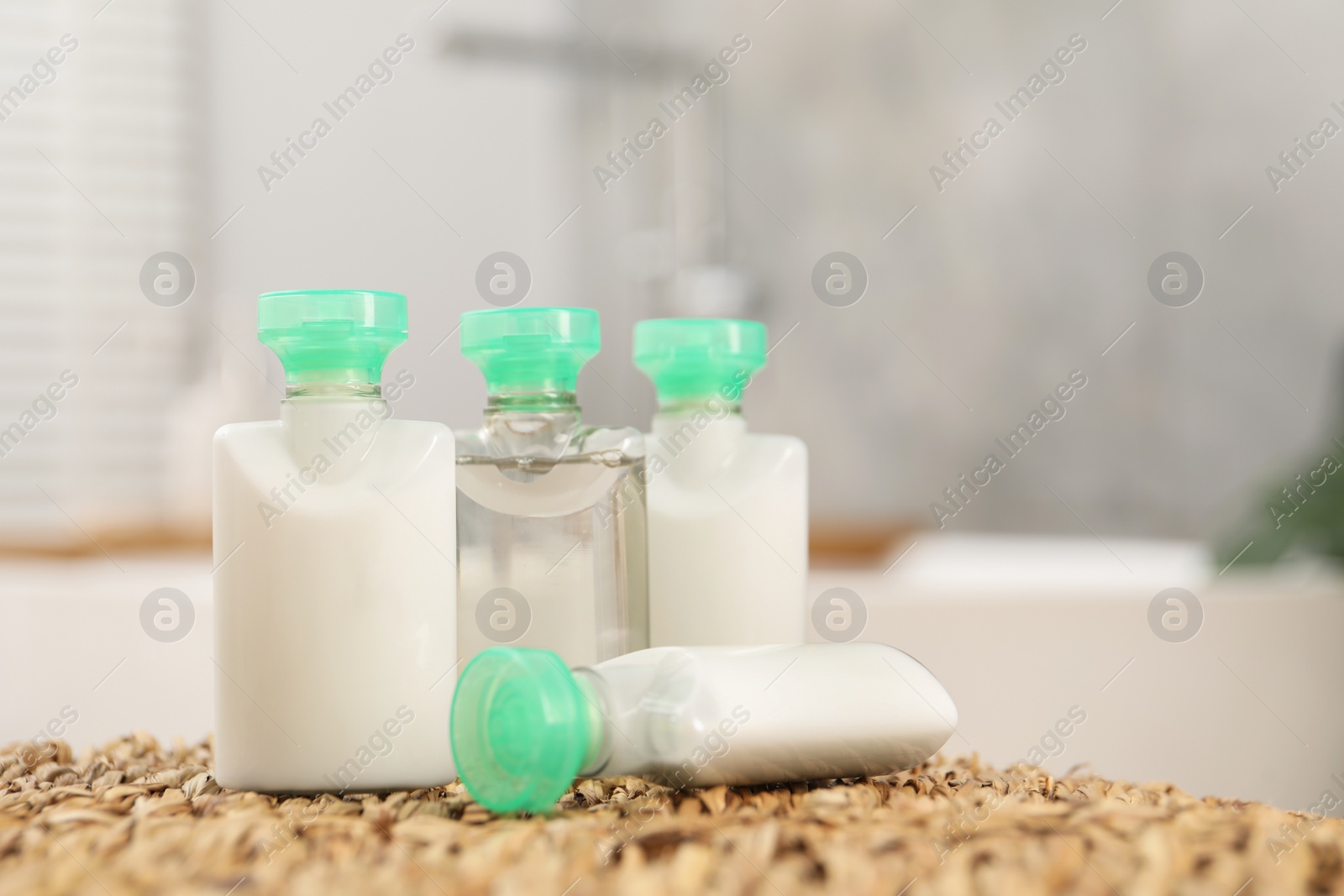 Photo of Mini bottles of cosmetic products on wicker mat against blurred background. Space for text