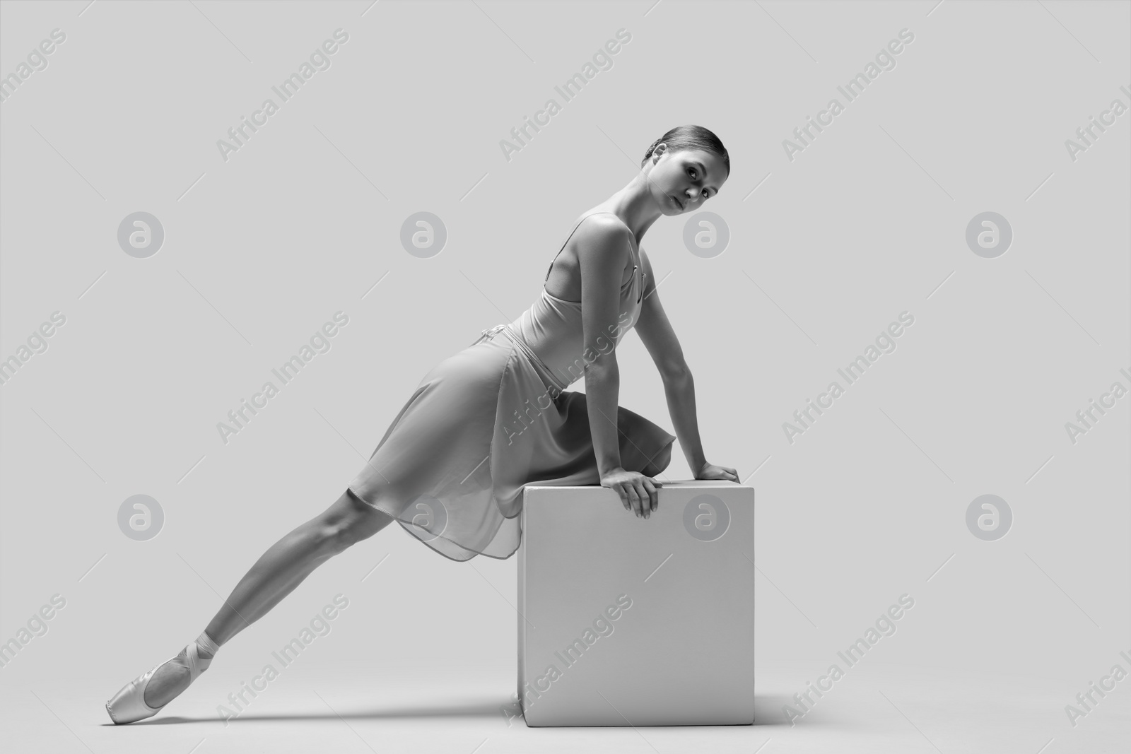 Photo of Young ballerina practicing dance moves on cube, toned in black and white