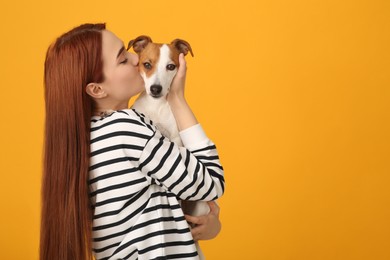 Photo of Woman kissing cute Jack Russell Terrier dog on orange background. Space for text