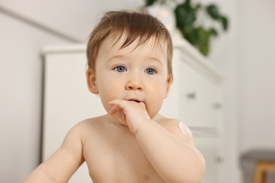 Cute little baby with moisturizing cream on body indoors