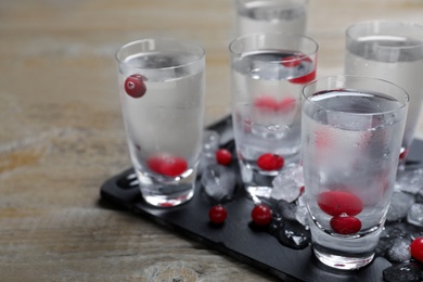 Shots of vodka, ice and cranberries on wooden table