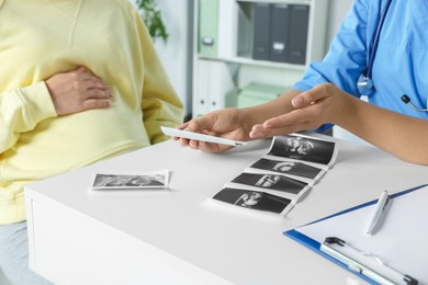 Photo of Doctor showing ultrasound picture to pregnant woman in clinic, closeup