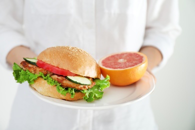 Photo of Woman holding plate with tasty sandwich and half of fresh grapefruit, closeup. Choice between diet and unhealthy food