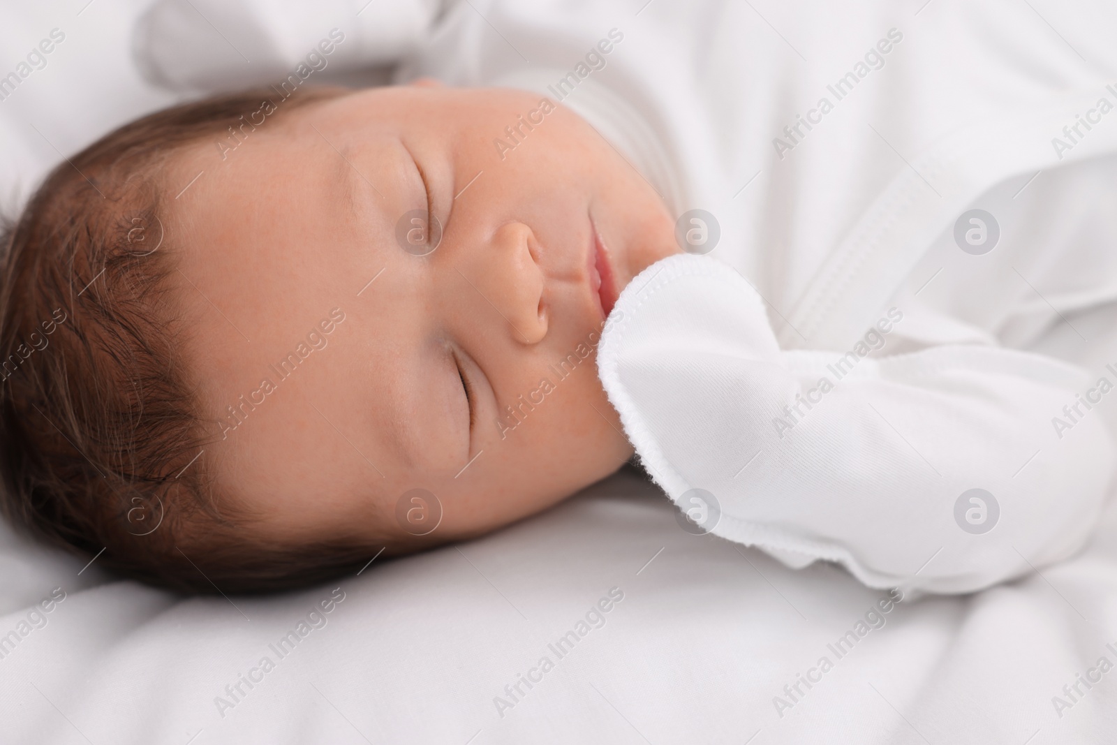 Photo of Cute newborn baby sleeping on white bed, closeup