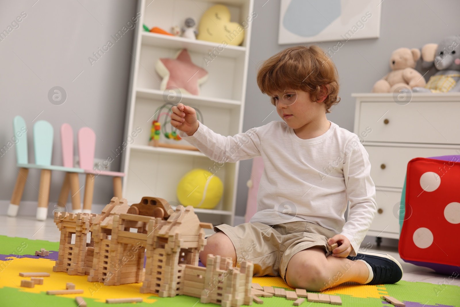 Photo of Little boy playing with wooden construction set on puzzle mat in room. Child's toy