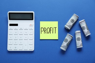 Photo of Sticky note with word Profit, rolled banknotes and calculator on blue background, flat lay