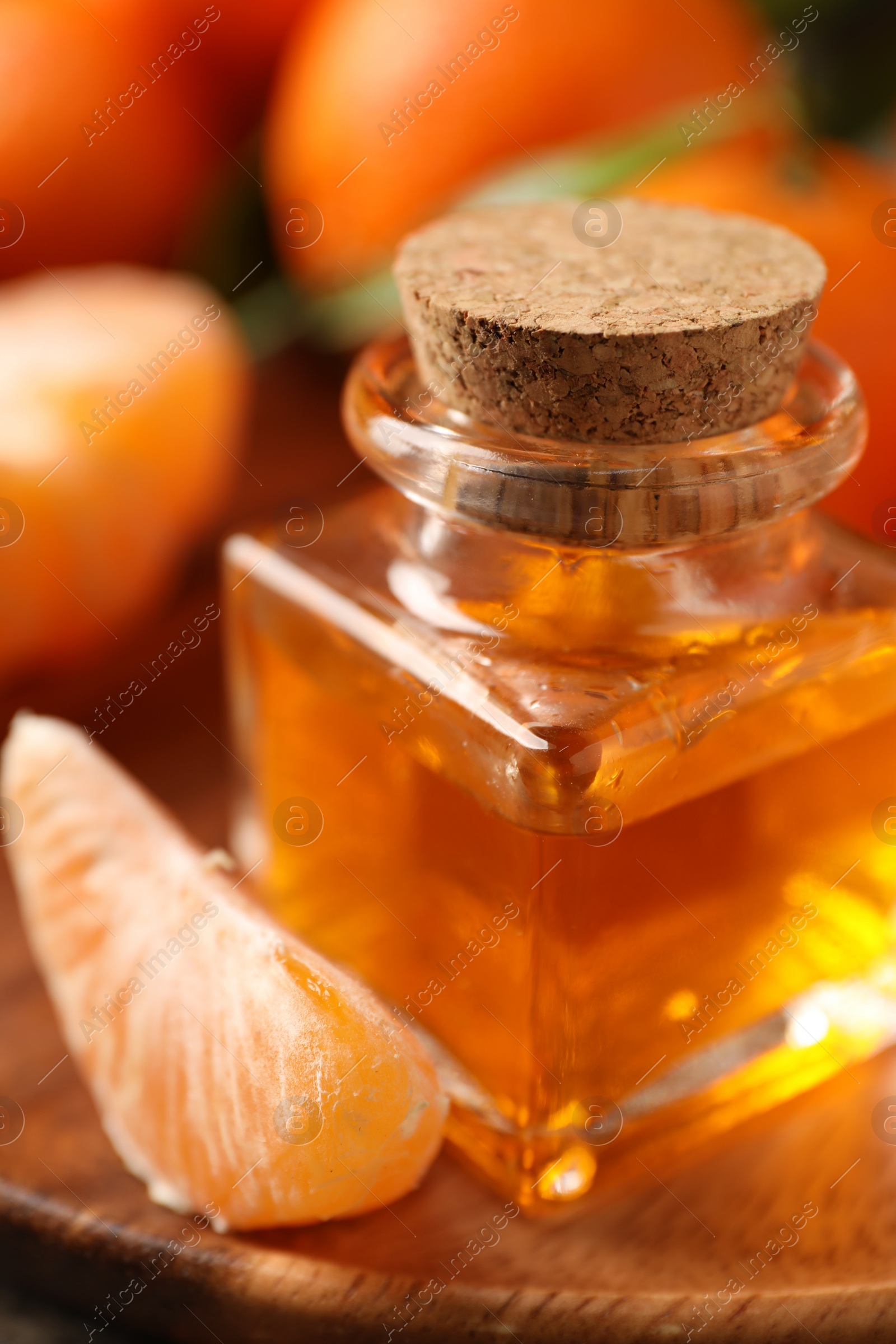 Photo of Bottle of tangerine essential oil and fresh fruits on wooden table, closeup