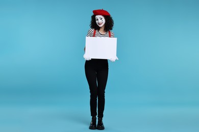Photo of Funny mime with blank sign posing on light blue background