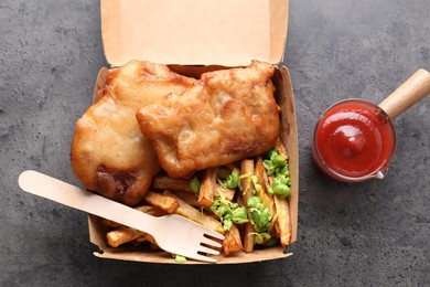 Photo of Tasty fish, chips, sauce and peas in paper box on grey table, top view