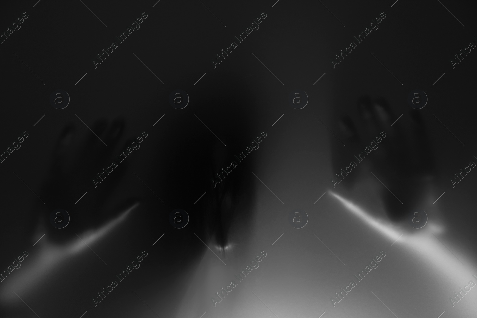 Photo of Silhouette of creepy ghost behind glass against grey background