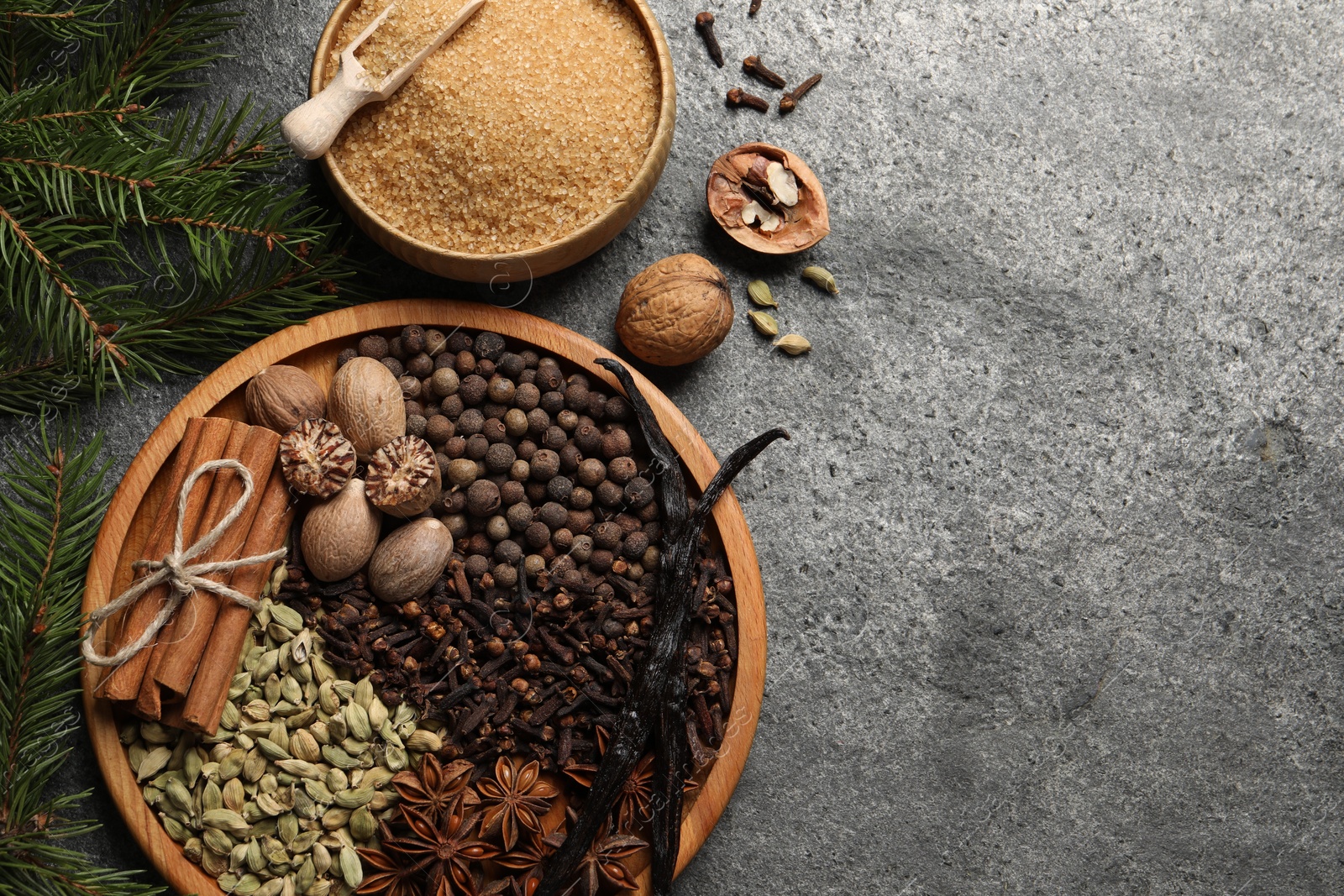 Photo of Different spices, nuts and fir branches on gray textured table, flat lay. Space for text