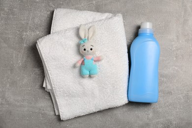 Photo of Bottle of laundry detergent, clean towel and rabbit toy on light grey table, flat lay