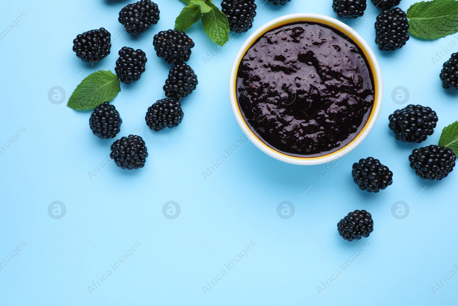 Photo of Blackberry puree in bowl and fresh berries on light blue background, flat lay. Space for text